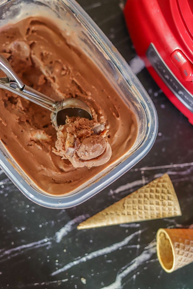 Nutella Ice Cream being scooped out of Tupperware with ice cream cones and ice cream maker in the background