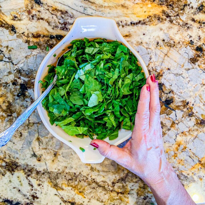 spinach in a bowl with a woman's hand on the side of the bowl