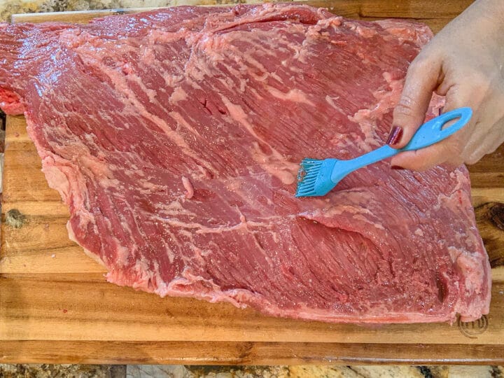 raw brisket being brushed with sauce