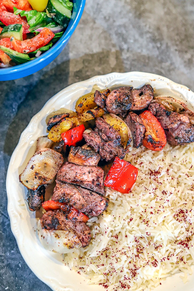 lamb shish kabobs and white rice with a salad in the background