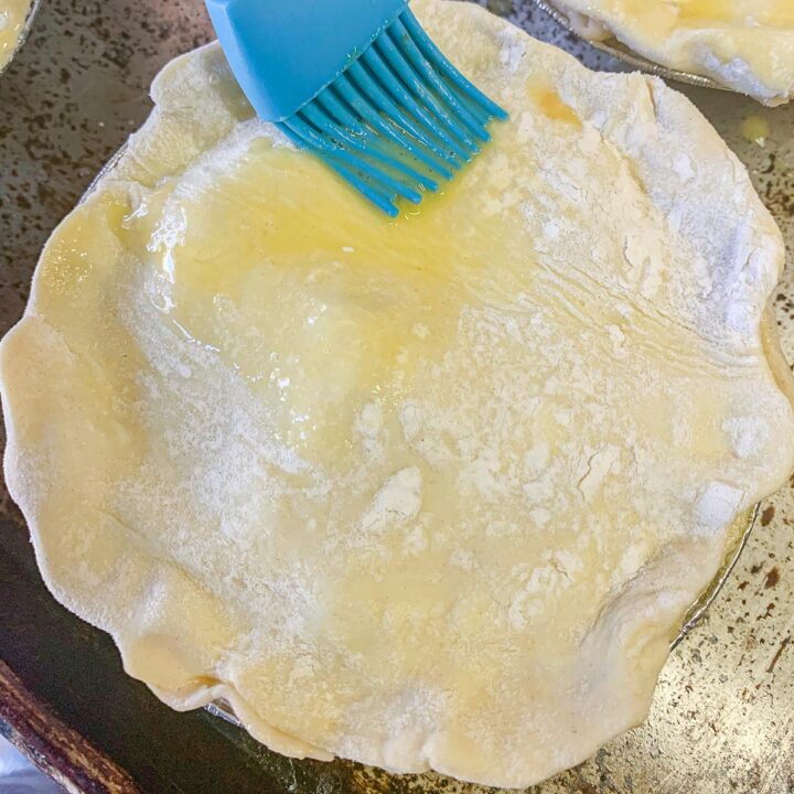 a mini pie being brushed with a blue rubber brush (meat pie recipe)