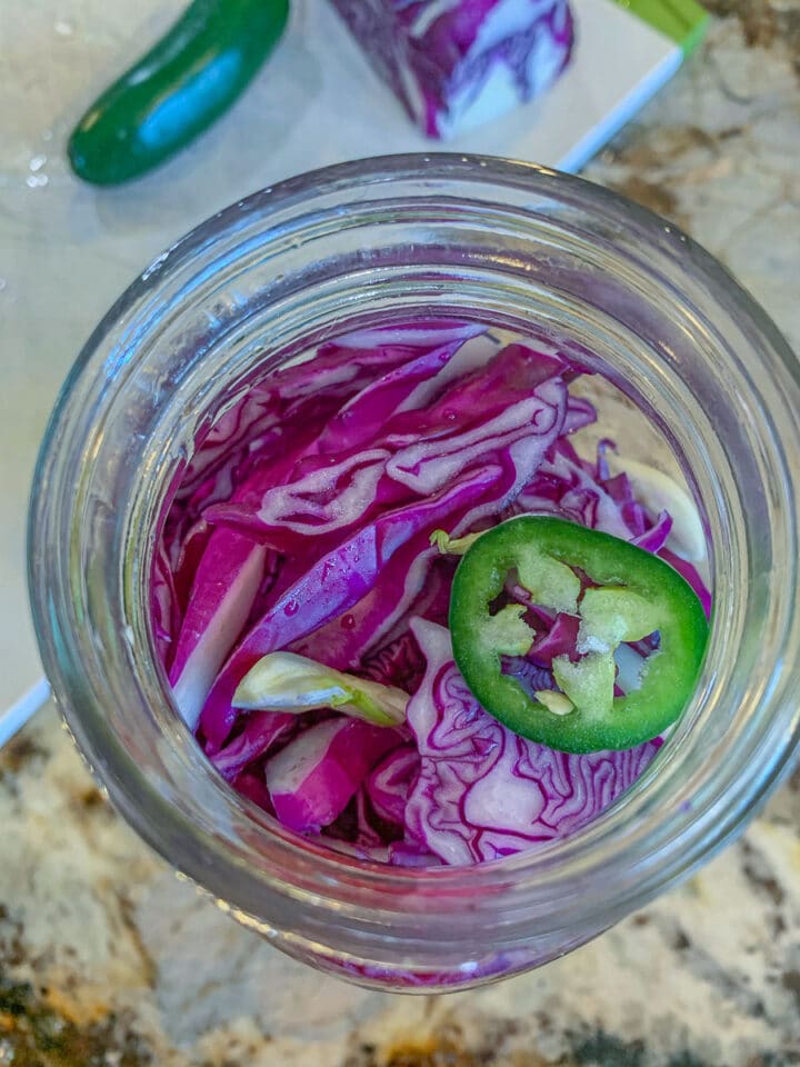 red cabbage in a jar topped with sliced jalapeño pepper
