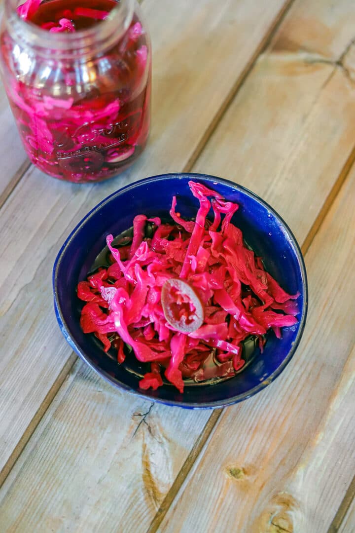 red pickled cabbage in a blue bowl and a bottle of pickled cabbage in the back