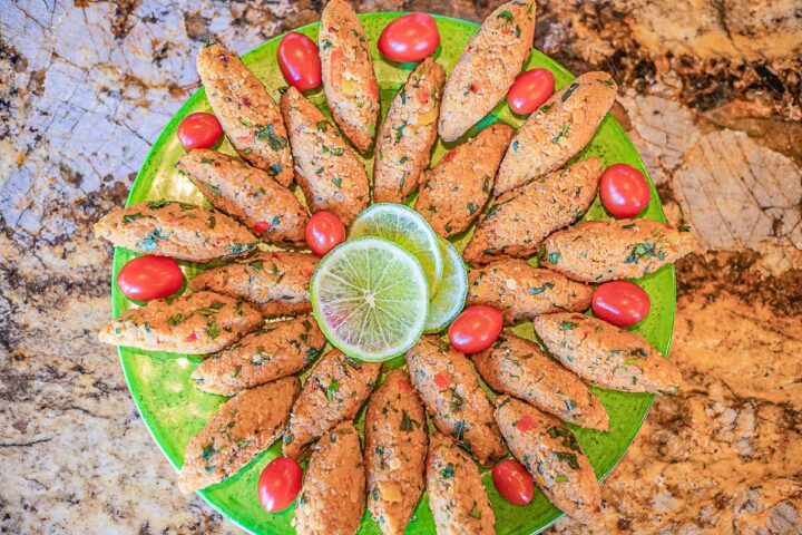 kibbeh (vegan lentil patties) on a plate with lime slices and grape tomatoes
