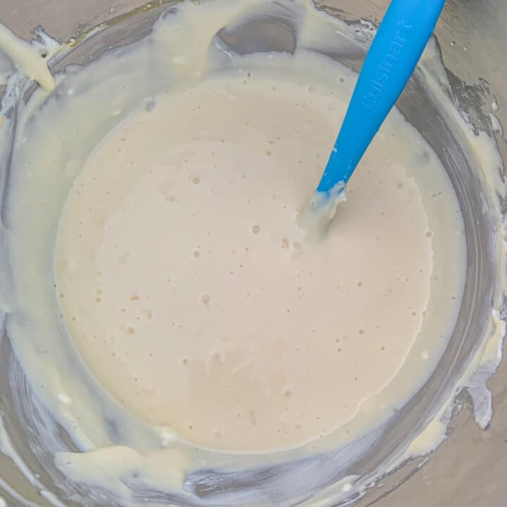 mulberry cheesecake batter in a mixing bowl with a blue spatula