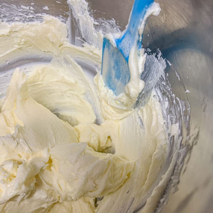 scraping the sides of a mixing bowl with cheesecake batter with a blue spatula
