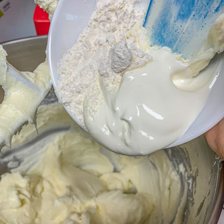 adding flour and sour cream into a mixing bowl with cream cheese