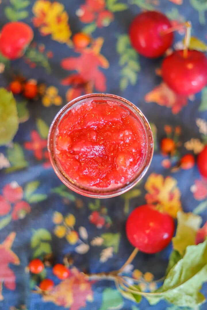 a jar of crabapple jam on a flowered surface