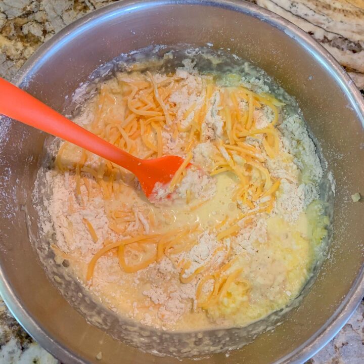 whisking shredded cheese into a silver bowl