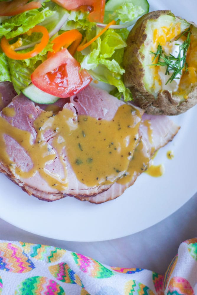 white plate with salad, baked potato, mustard sauce and ham