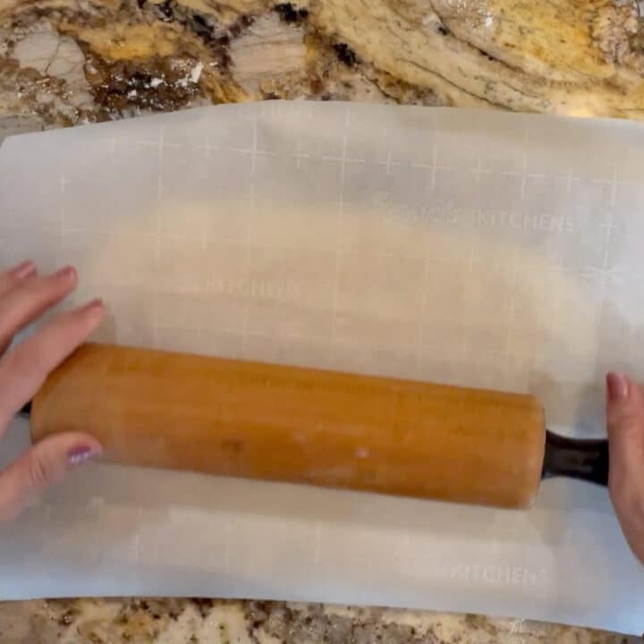 Nazook dough covered with parchment paper and being rolled by rolling pin
