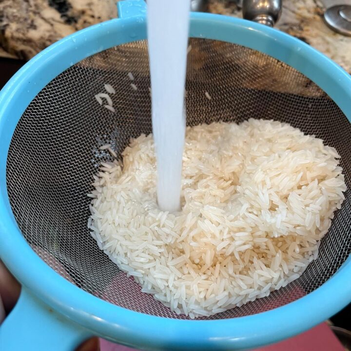 rice being washed in a a blue strainer