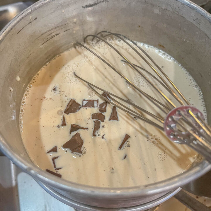 milk and chocolate chips in a pan with a whisk in the center