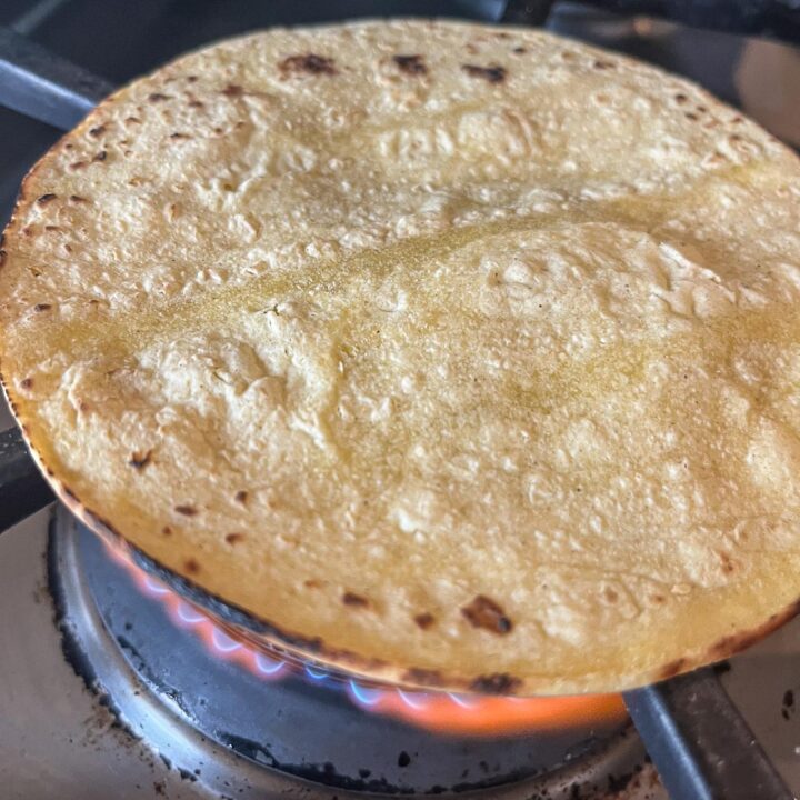 corn tortilla being charred on a gas flame