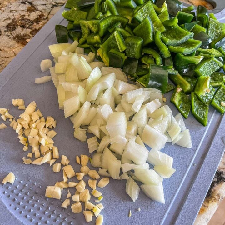 chopped onions, peppers, and garlic on a blue cutting board