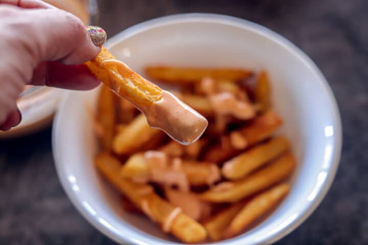 French fries in a white bowl with one dipped in sriracha aioli