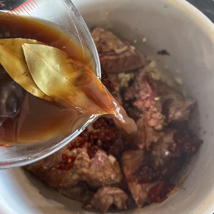 pouring broth mix over pork neck bones in a pot