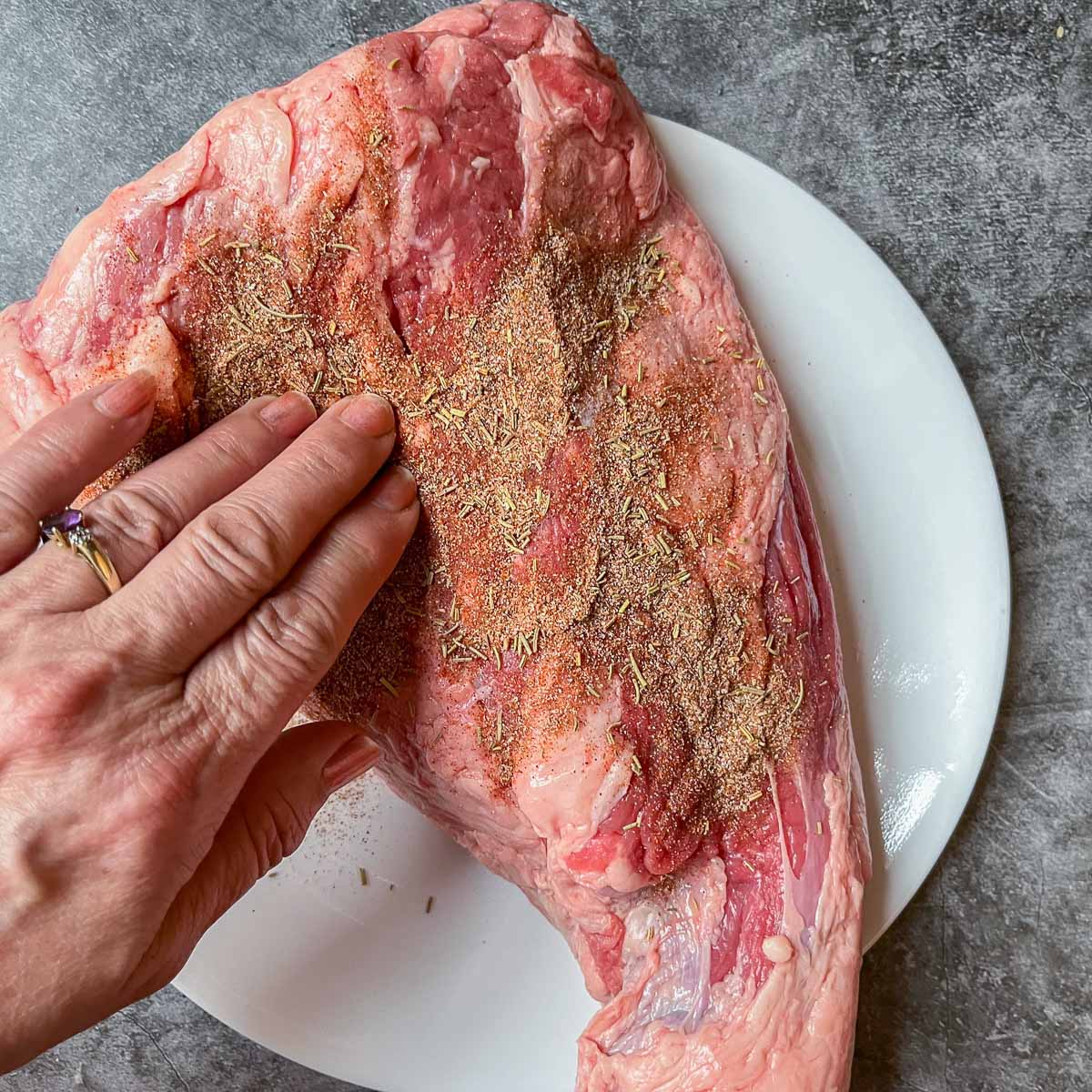 rubbing dry rub into a raw trig-tip roast