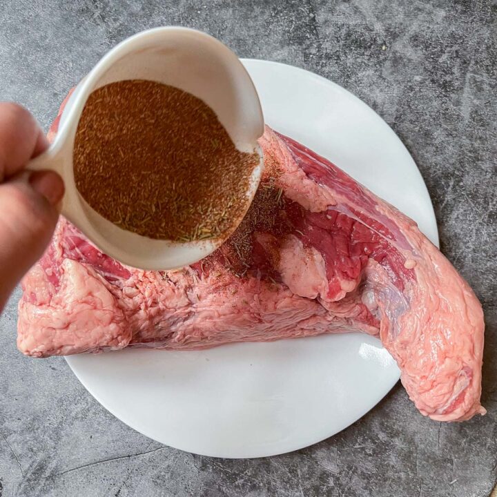 pouring dry rub over a raw tri-tip