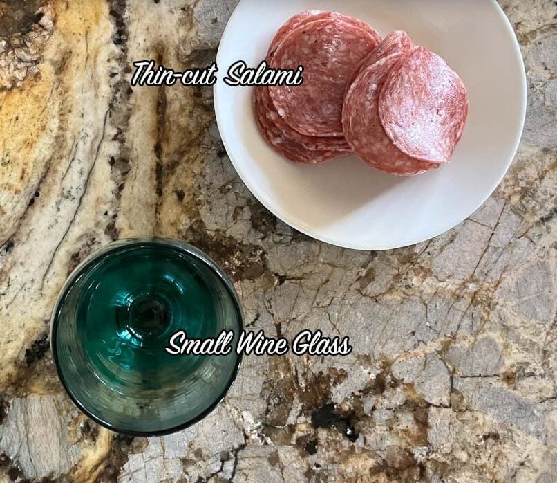 salami rose ingredients including salami on a white plate and a wine glass.