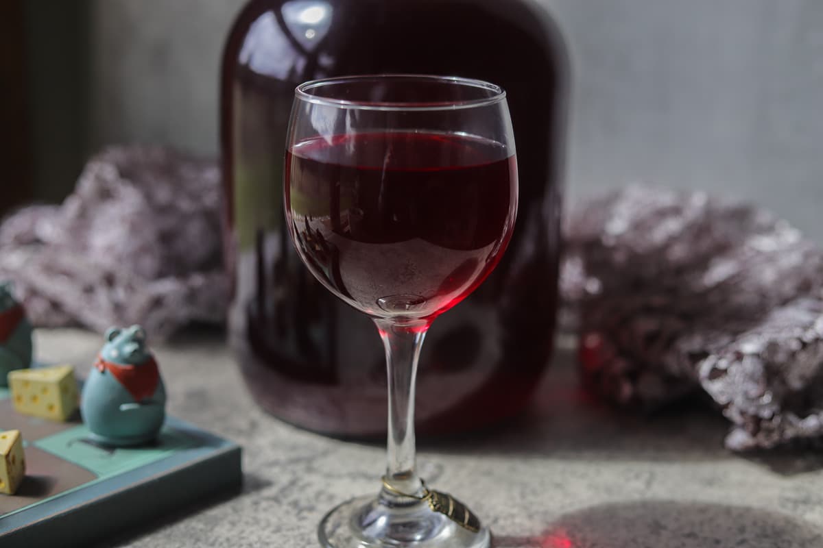gallon of chokecherry wine with a a glass of wine in front of it