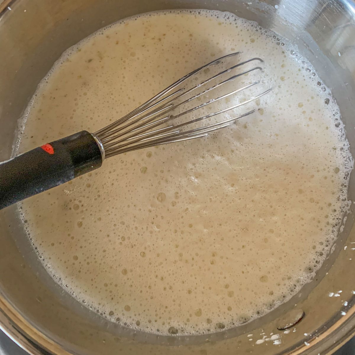whisking middle eastern milk pudding in a silver pot