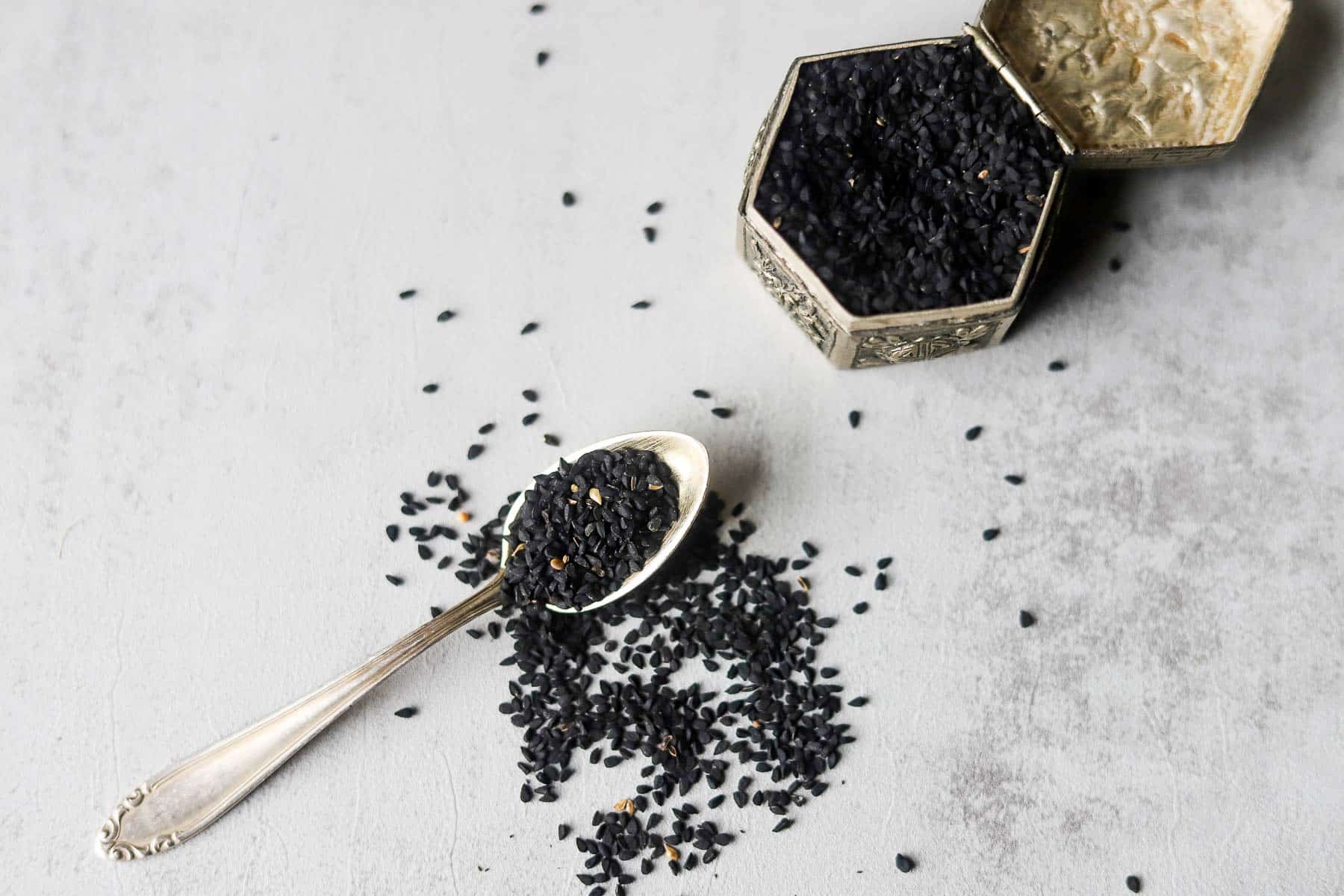 a spoon and silver snuff box filled with nigella seeds