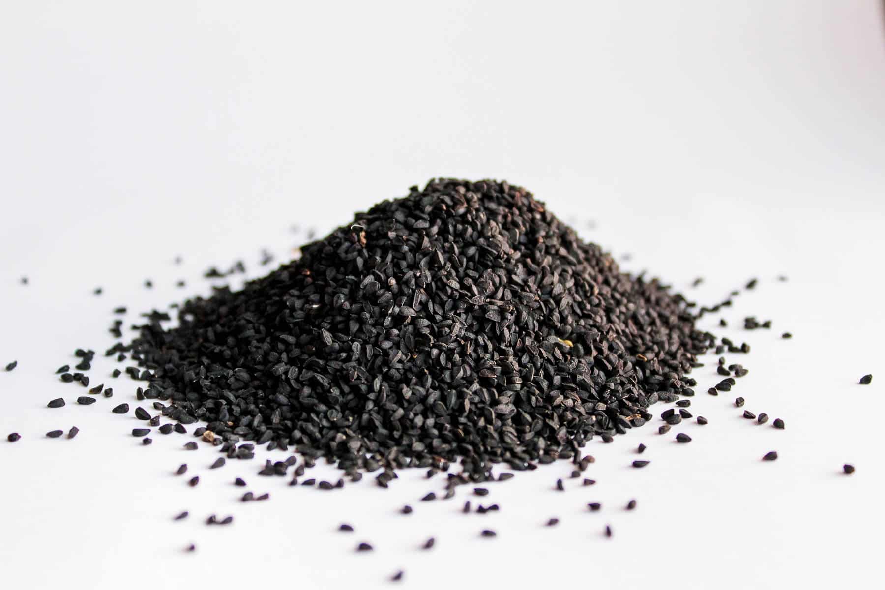 a pile of black nigella seeds against a white background