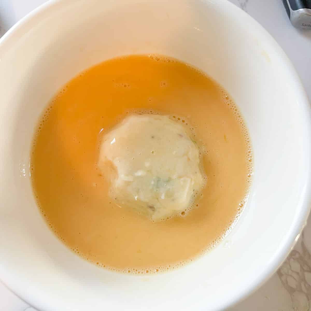 potato ball in a bowl of whisked egg