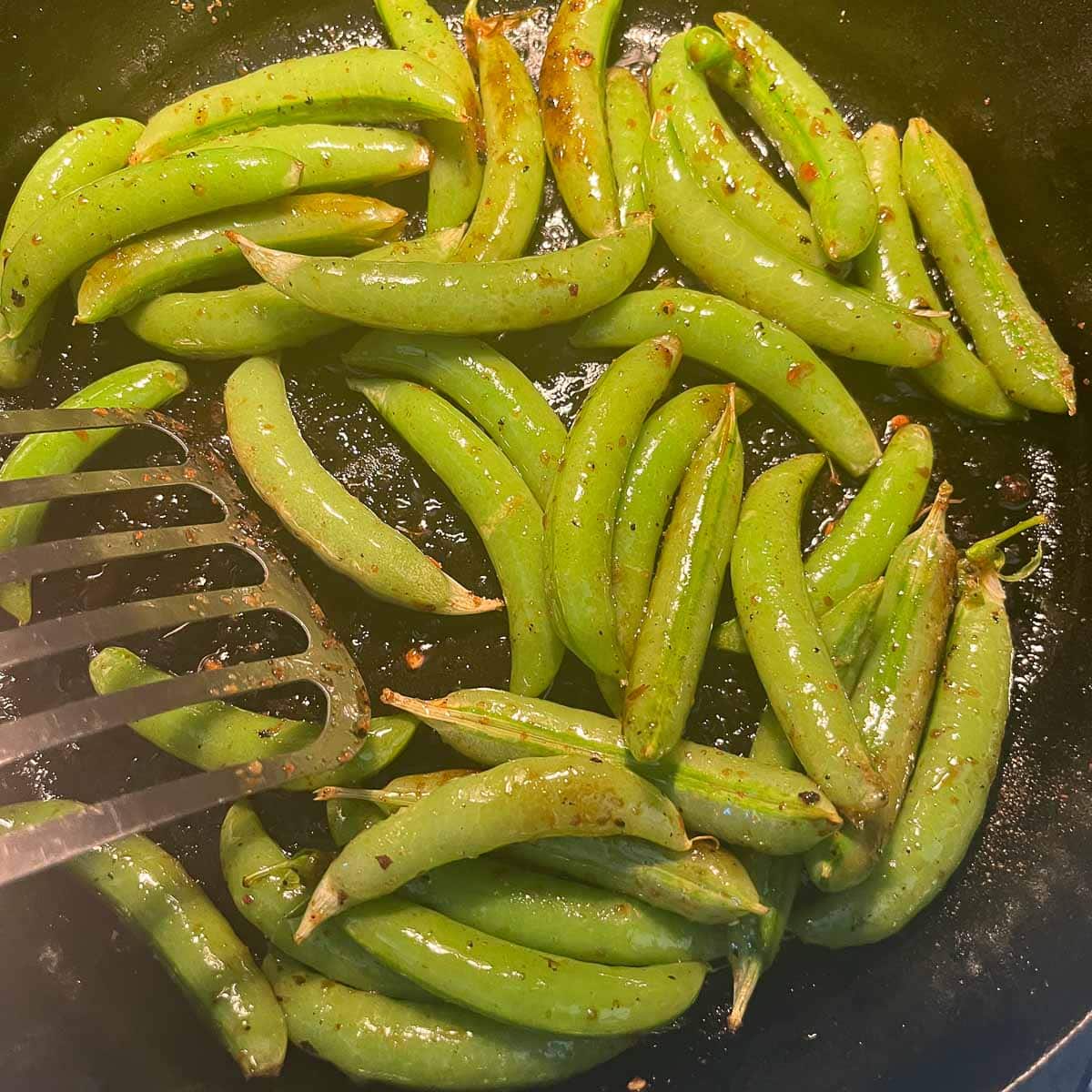 stirring snap peas in a pan with a metal spatula