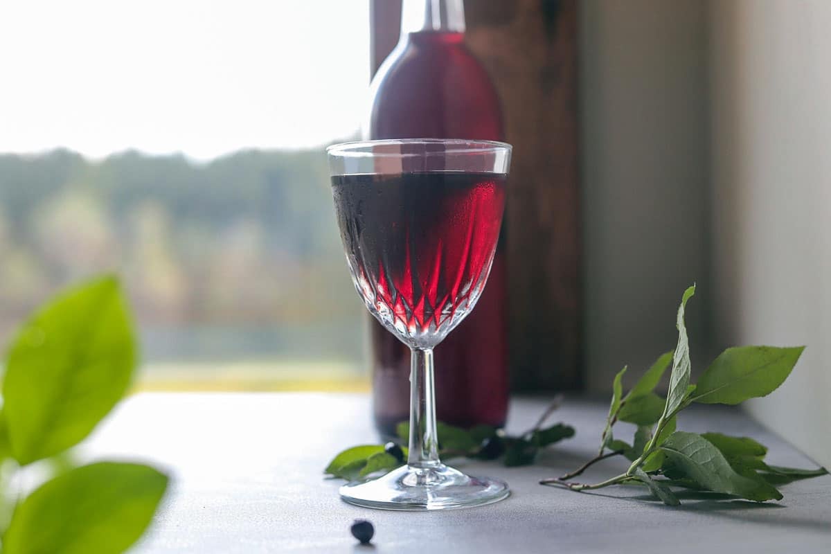 huckleberry wine in a glass with a bottle behind it