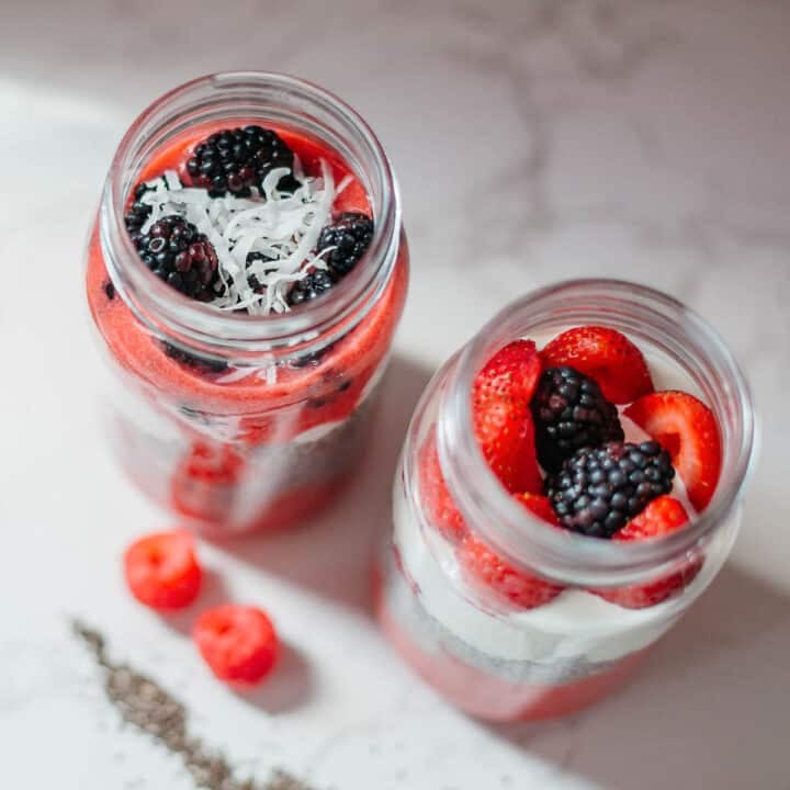 high protein chia seed pudding in two mason jars with fresh berries and shredded coconut