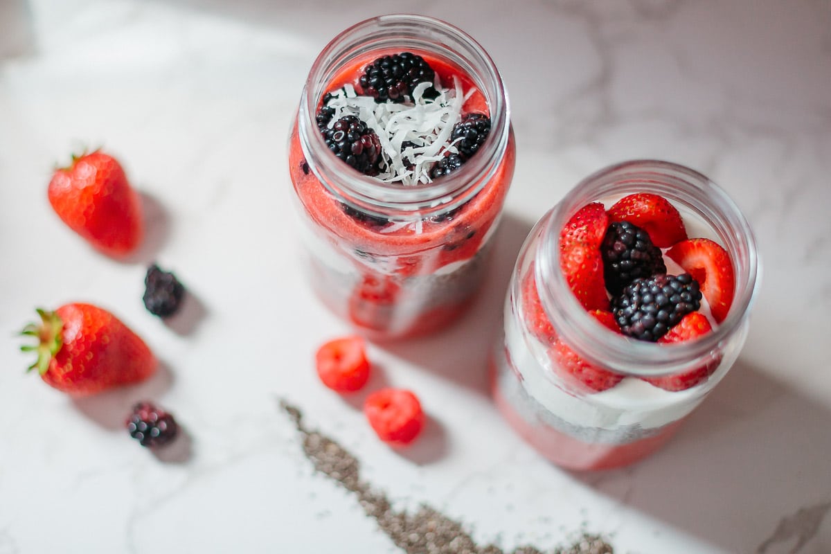 high protein chia seed pudding in two mason jars with fresh berries and shredded coconut