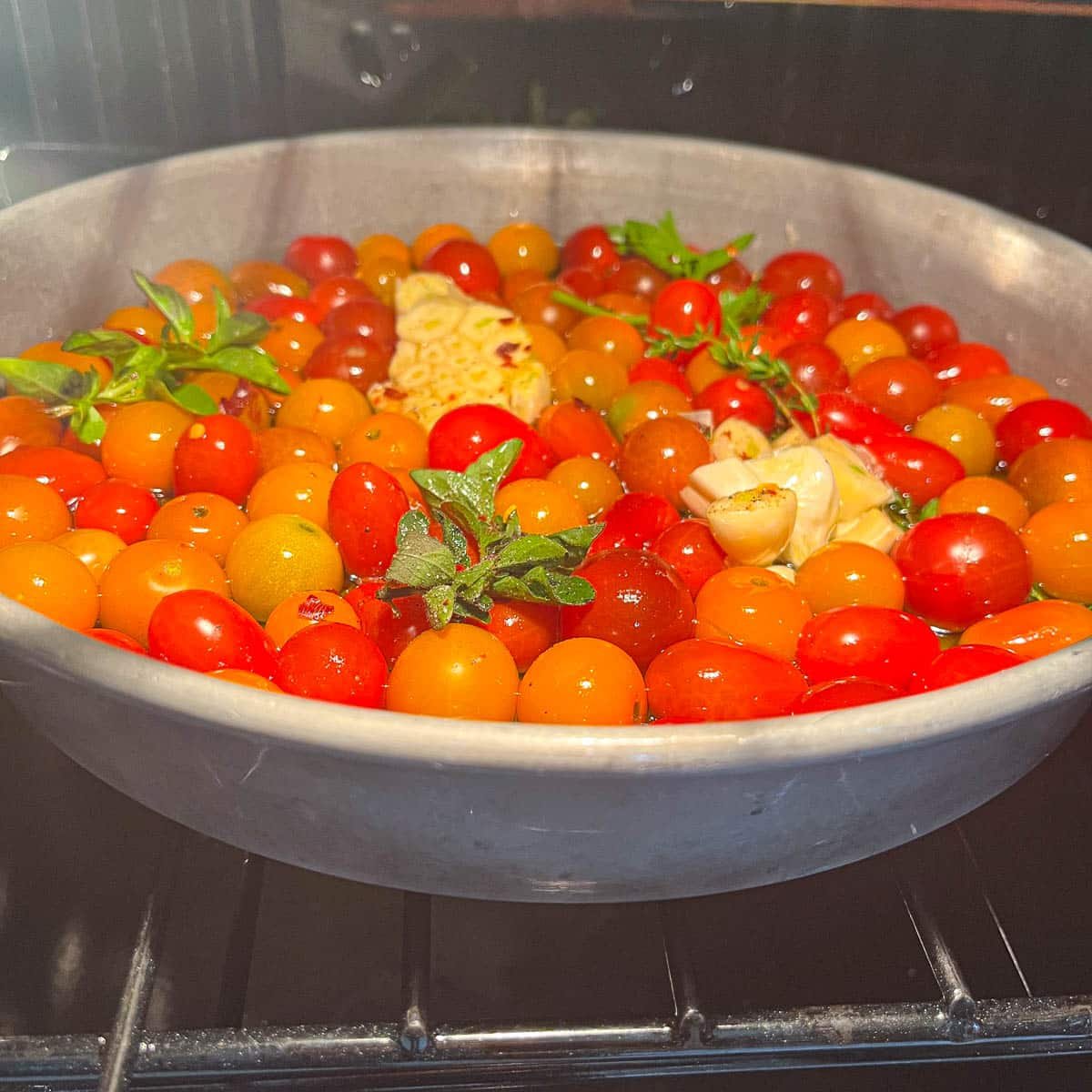 cherry tomatoes, garlic, and herbs in a pan in the oven