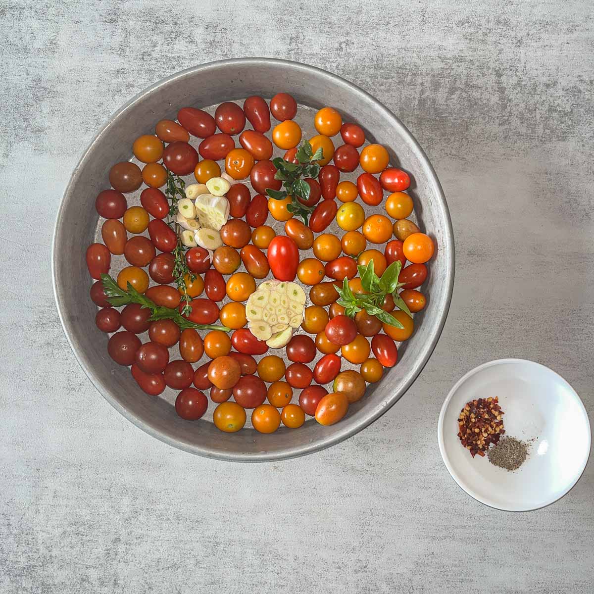 a round pan with cherry tomatoes, garlic and herbs