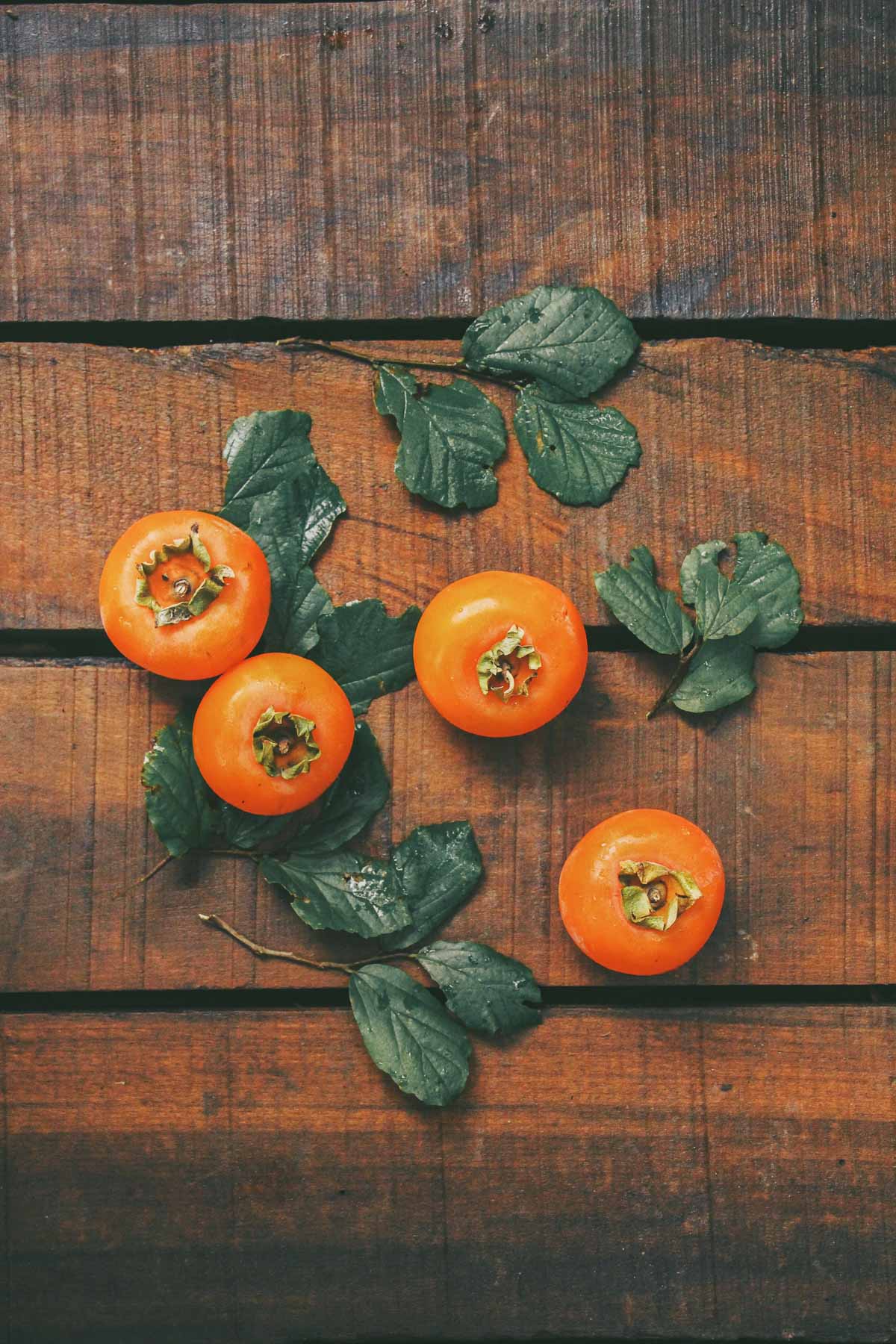 persimmons and leaves on a wooden background