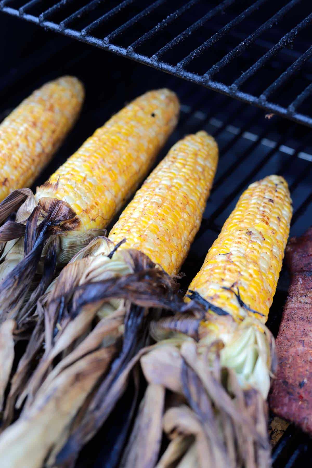 four corn on the cob being smoked on a traeger grill