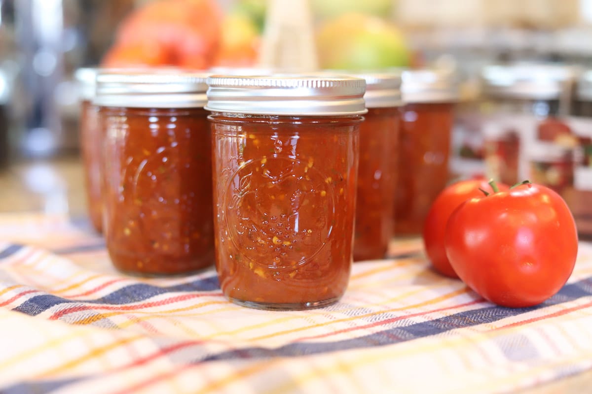 canned salsa on the counter with tomatoes around the jars