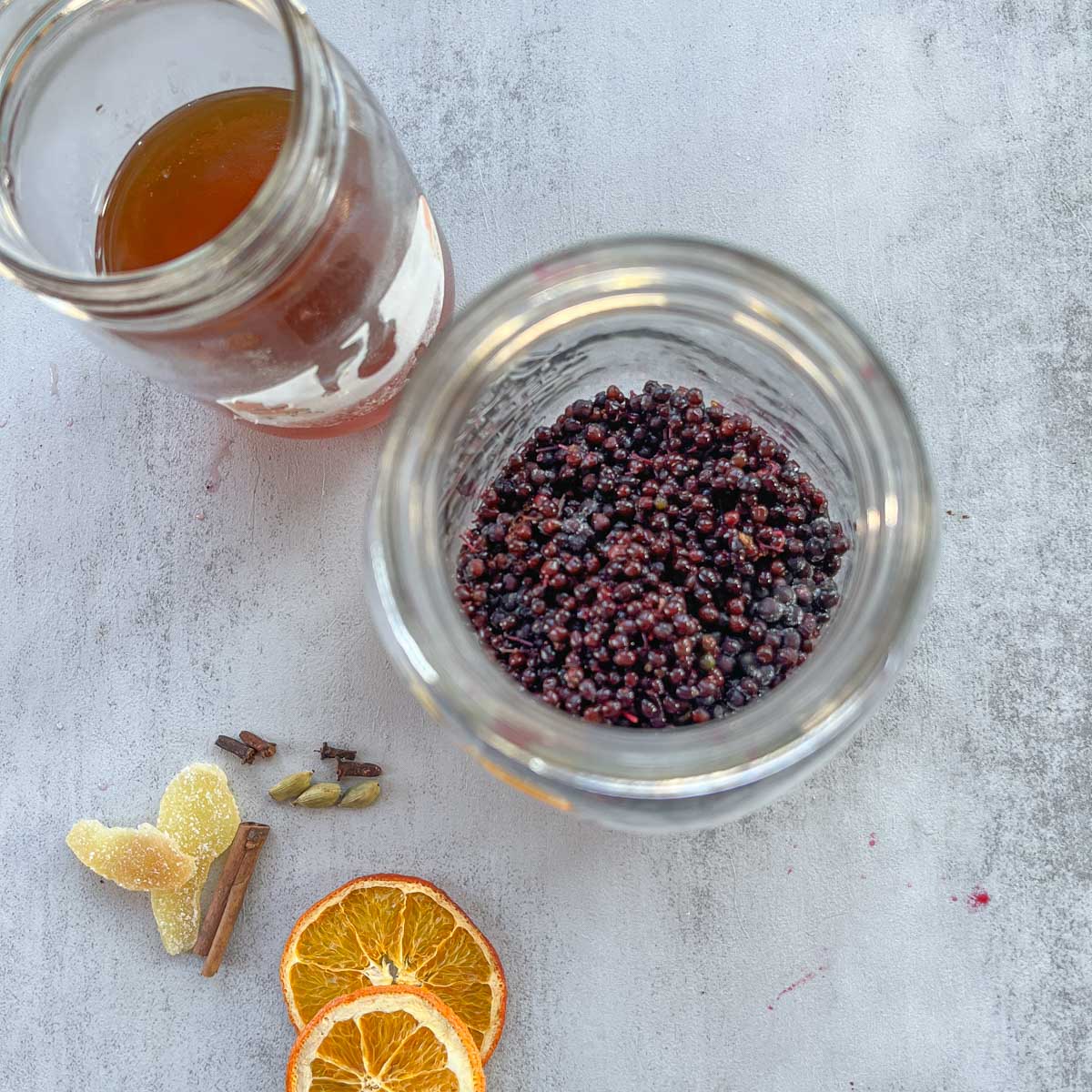 elderberries in a jar with spices and vinegar next to it