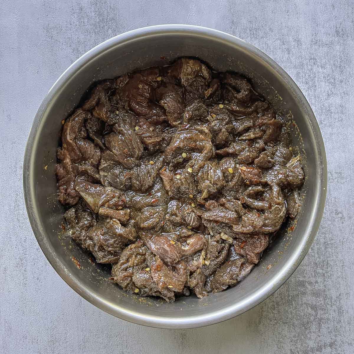 raw elk meat being marinated in a bowl