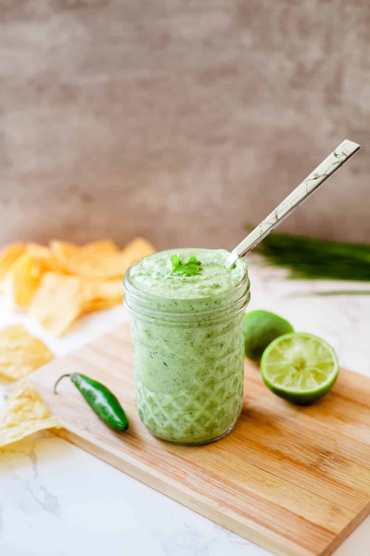 cilantro lime sauce in a jar beside limes serrano and chips