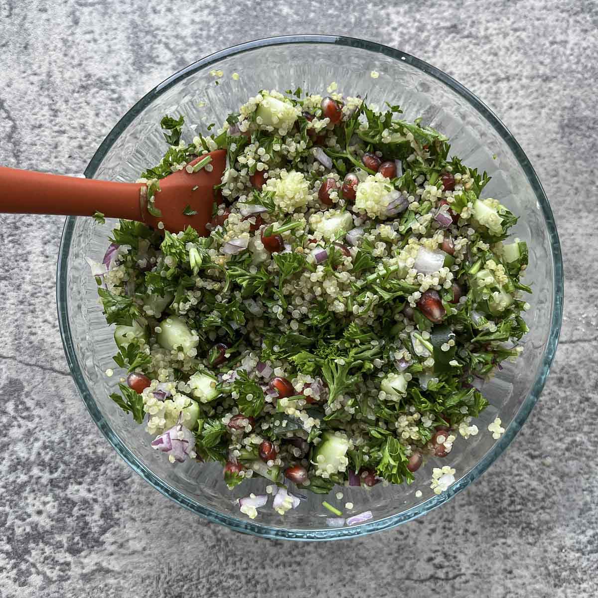 zesty quinoa salad in a salad bowl with a red spatula