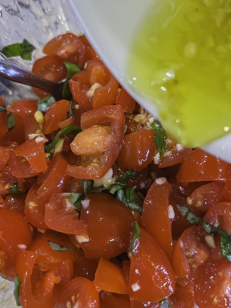 preparing bruschetta caprese by adding olive oil to chopped tomatoes and basil