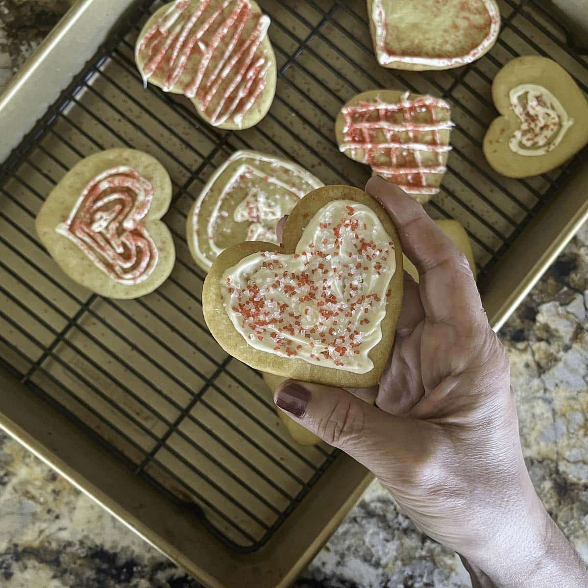 a heart shaped cookies being held over a tray of more cookies