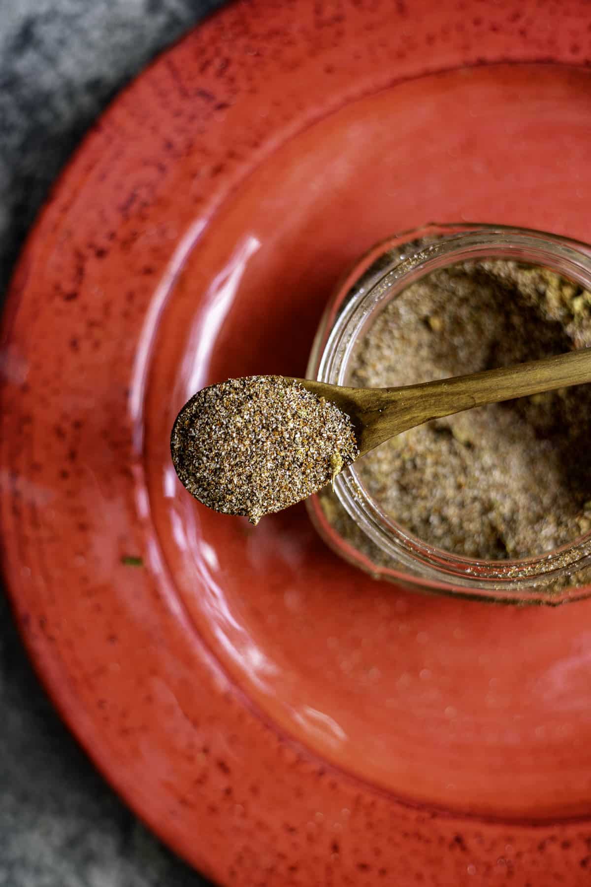 carne asada seasoning in a spoon over a jar on a red plate