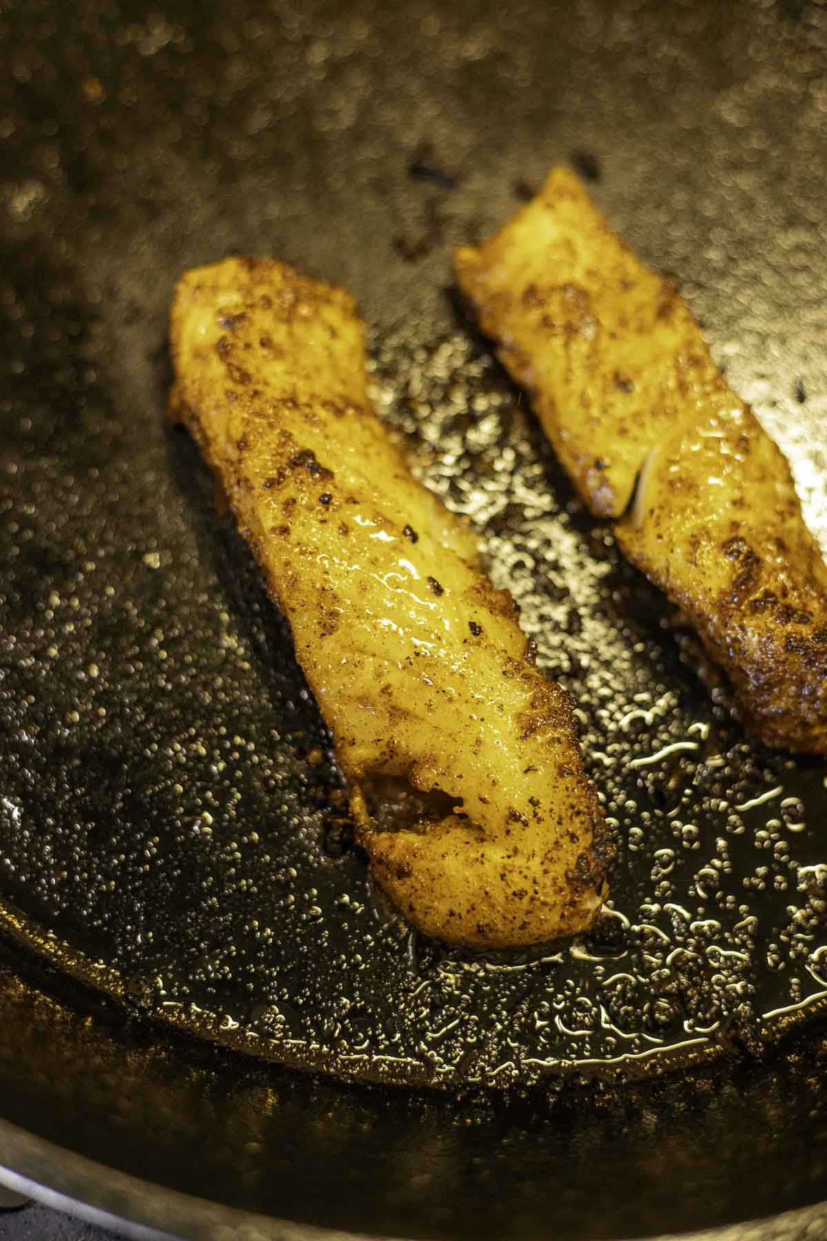 blackened fish frying in a pan