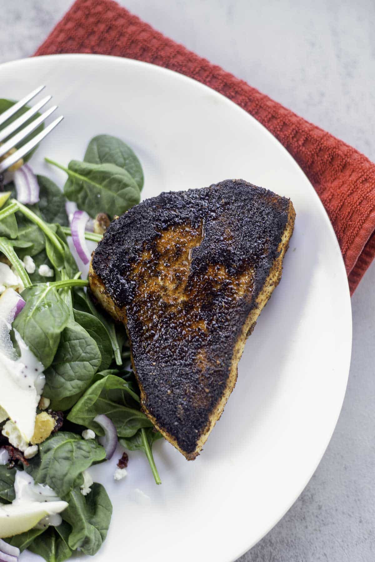 blackened swordfish on a white plate with a salad on the side