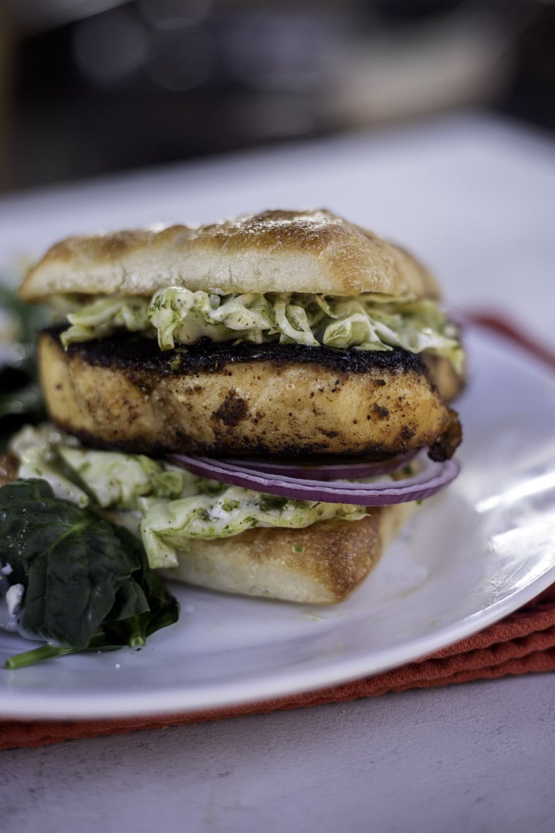 blackened swordfish sandwich on a white plate over a red napkin