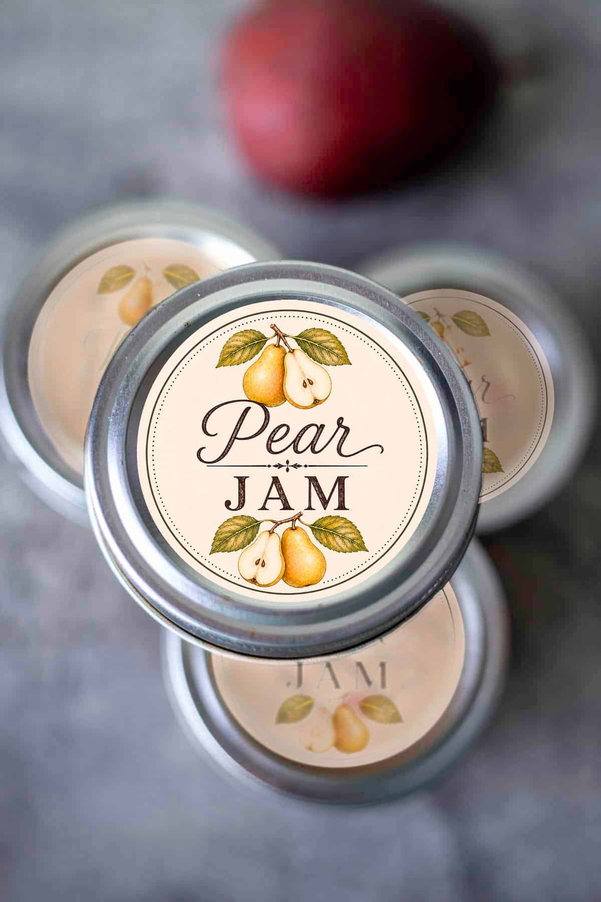 jars of pear jam stacked on one another with a red pear in the background.