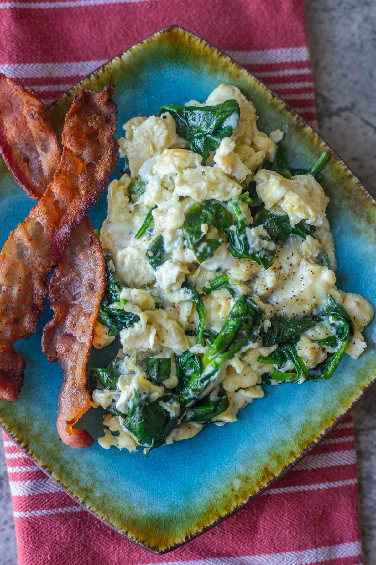 spinach and eggs with bacon on a blue plate